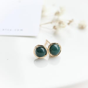 Peut inclure: Une paire de boucles d'oreilles en or avec une pierre vert foncé dans chacune. Les pierres sont serties dans un cercle d'or.