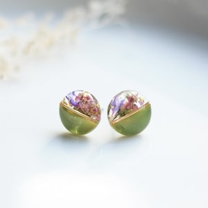 Op de afbeelding: Een paar groene en gouden oorbel studs met geperste bloemen erin. De bloemen zijn paars en roze.
