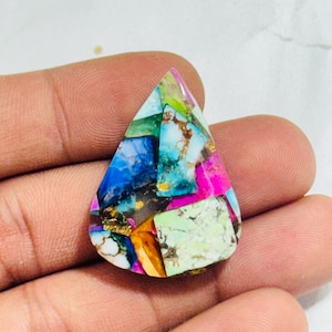 May include: A teardrop-shaped gemstone mosaic with a vibrant mix of colors, including blue, pink, green, and gold. The stone is held in a hand, showcasing its unique, irregular pattern and polished surface. This gemstone is ideal for jewelry making.