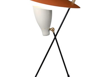 May include: A mid-century modern table lamp with a white, cone-shaped shade and a copper-colored, curved top. The lamp has a black, crossed-leg base and a gold-colored accent. The lamp is designed to provide focused lighting.