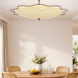 May include: A retro-style ceiling light fixture with a cream-colored, scalloped shade and a dark red trim. The light is suspended from a matching red canopy. The image also shows a round wooden dining table with four chairs, a vase of flowers, and a bowl of lemons.