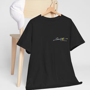 Può includere: T-shirt nero con la scritta "Limited Edition" in un carattere corsivo multicolore. Un berretto da baseball bianco poggia sullo schienale di una sedia di legno. La maglietta è appesa a una gruccia di legno.
