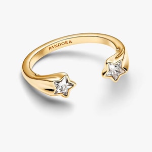 Pode incluir: Um anel dourado com um design aberto, apresentando dois detalhes em forma de estrela, cada um com uma pedra clara e brilhante. A palavra "PANDORA" está gravada na banda. Uma joia elegante.