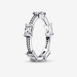May include: A silver ring with multiple clear rectangular and round-cut stones. The ring features a band with small, round stones and larger rectangular stones set around the band. The ring is designed with a modern, elegant style.