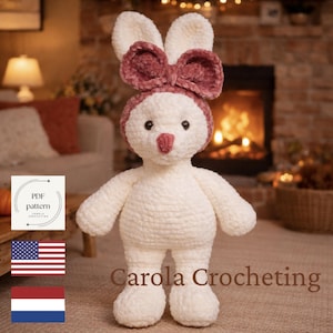 Op de afbeelding: Een handgemaakt, crèmekleurig gehaakt konijn met een mauve strik en hoofdband. Het konijn heeft zwarte ogen en een roze neus. De tekst "Carola Crocheting" is zichtbaar. De afbeelding bevat ook een PDF-patroonlogo, de Amerikaanse vlag en de Nederlandse vlag.