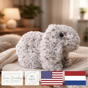 Op de afbeelding: Een zacht, grijs en wit konijn met slappe oren, rustend op een crèmekleurige gebreide deken. Het konijn heeft een zachte textuur. De afbeelding bevat de tekst "Carola Crocheting PDF Pattern" en de Amerikaanse vlag.