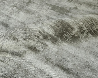 May include: A close-up shot of a textured, gray rug with a subtle, distressed pattern. The rug's surface has a soft, velvety appearance, with visible linear striations and areas of lighter and darker gray tones, creating a sense of depth and dimension.