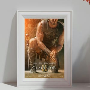 Könnte beinhalten: Ein gerahmtes Filmplakat für "Gladiator II" mit einem knienden Gladiator mit einem Schwert. Das Poster hat eine warme Farbpalette mit dem Filmtitel und den Namen der Schauspieler. Das Erscheinungsdatum, der 22. November, ist ebenfalls angegeben.