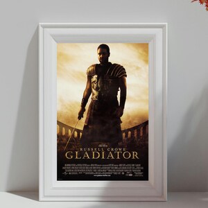 Könnte beinhalten: Gerahmtes Filmplakat für den Film "Gladiator" mit Russell Crowe. Das Poster hat einen sepiafarbenen Hintergrund mit dem Titel in goldener Schrift. Das Bild zeigt Crowe in Gladiatorenrüstung mit einem Schwert.