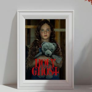 Puede incluir: Una impresión enmarcada que muestra a una persona con cabello largo y rizado sosteniendo un oso de peluche gris. El texto HOLY GHOST está impreso en letras rojas en negrita en el centro de la imagen. El marco es blanco con moldura clásica.