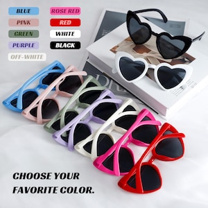 Può includere: Una collezione di occhiali da sole a forma di cuore in vari colori: blu, rosa, verde, viola, bianco, nero e rosso. L'immagine include anche il testo "CHOOSE YOUR FAVORITE COLOR."