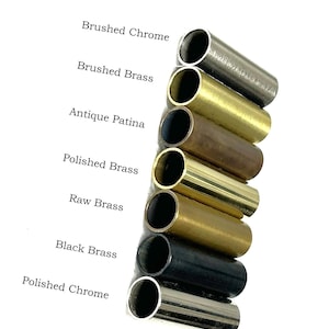 K&ouml;nnte beinhalten: Eine vertikale Anordnung von sieben zylindrischen Metallrohren in verschiedenen Ausf&uuml;hrungen, beschriftet als Brushed Chrome, Brushed Brass, Antique Patina, Polished Brass, Raw Brass, Black Brass und Polished Chrome, die unterschiedliche Metalltexturen zeigen.