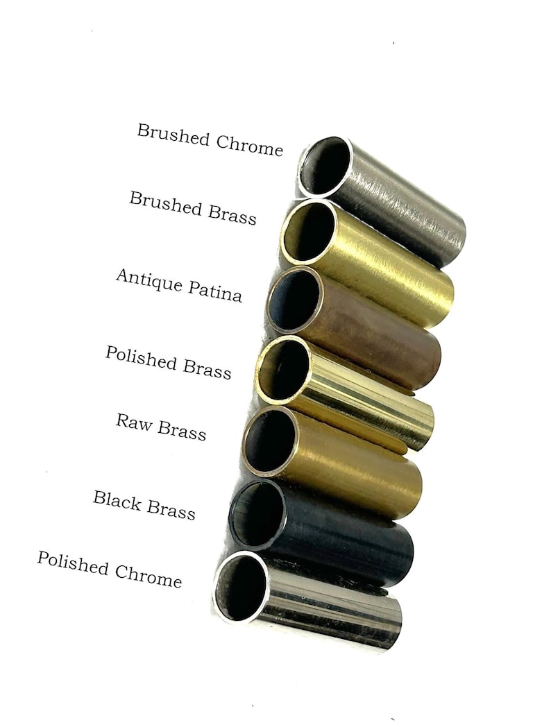 K&ouml;nnte beinhalten: Eine vertikale Anordnung von sieben zylindrischen Metallrohren in verschiedenen Ausf&uuml;hrungen, beschriftet als Brushed Chrome, Brushed Brass, Antique Patina, Polished Brass, Raw Brass, Black Brass und Polished Chrome, die unterschiedliche Metalltexturen zeigen.