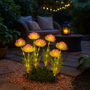 Op de afbeelding: Een cluster van verlichte kunstbloemen met gele en roze bloemblaadjes, geplaatst in een tuin. De op zonne-energie werkende lichten creëren een warme gloed, waardoor de sfeer in de buitenlucht wordt versterkt. De bloemen zijn gerangschikt tussen groen gebladerte.