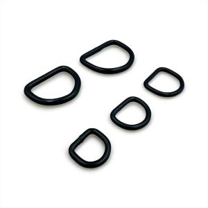May include: Five black D-rings are displayed against a white backdrop. Each ring has a rounded D-shape. The rings are made of a solid, opaque material. The sizes of the rings vary slightly, with a consistent design.