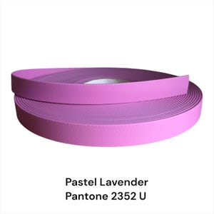 Puede incluir: Un rollo de cinta lavanda pastel, con una superficie texturizada, se muestra sobre un fondo blanco. La cinta es de un color p&uacute;rpura suave y apagado. El texto "Pastel Lavender Pantone 2352 U" est&aacute; en la parte inferior de la imagen.