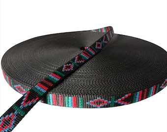 May include: A roll of black webbing with a decorative patterned strap. The strap features a repeating design in red, blue, and green. The webbing is tightly wound, creating a circular shape.