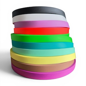 Puede incluir: Una pila de bandas curvas de colores, que van del negro al blanco, pasando por el rosa, el rojo, el verde, el turquesa, el amarillo, el marrón y el morado. Las bandas están apiladas ordenadamente, mostrando un espectro de colores vivos. Las bandas parecen estar hechas de un material flexible.