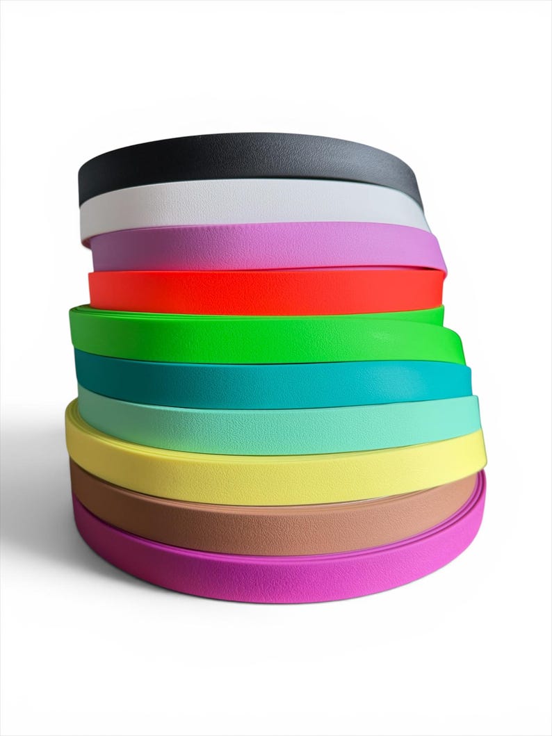 Puede incluir: Una pila de bandas curvas de colores, que van del negro al blanco, pasando por el rosa, el rojo, el verde, el turquesa, el amarillo, el marr&oacute;n y el morado. Las bandas est&aacute;n apiladas ordenadamente, mostrando un espectro de colores vivos. Las bandas parecen estar hechas de un material flexible.