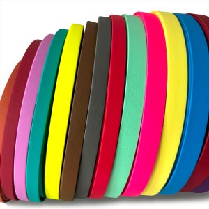 Può includere: Una collezione di strisce di cuoio colorate, disposte in un motivo curvo a forma di onda. Le strisce mostrano una varietà di colori vivaci, tra cui rosso, rosa, giallo, verde e blu. I bordi delle strisce sono visibili, creando un aspetto strutturato.