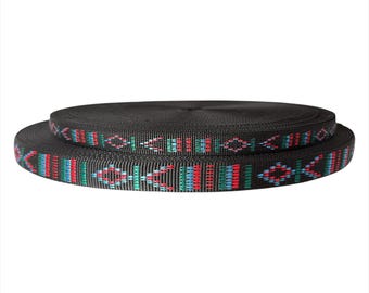 May include: Two rolls of black webbing with a colorful geometric pattern. The pattern includes red, blue, and green accents. The rolls are stacked on top of each other, with the top roll slightly smaller than the bottom roll.