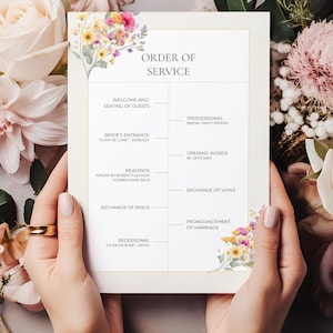 Puede incluir: Una tarjeta de orden de servicio de boda sostenida por manos, rodeada de arreglos florales. La tarjeta presenta texto, incluyendo "Orden de servicio", y detalles de la ceremonia. El diseño incluye acentos florales y bordes dorados.