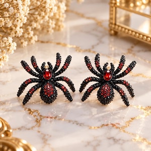 May include: A pair of spider-shaped earrings featuring black and red crystals. Each spider has a central oval red stone on its back, with smaller red crystals accenting the legs and body, while the rest of the structure is covered in black beads.