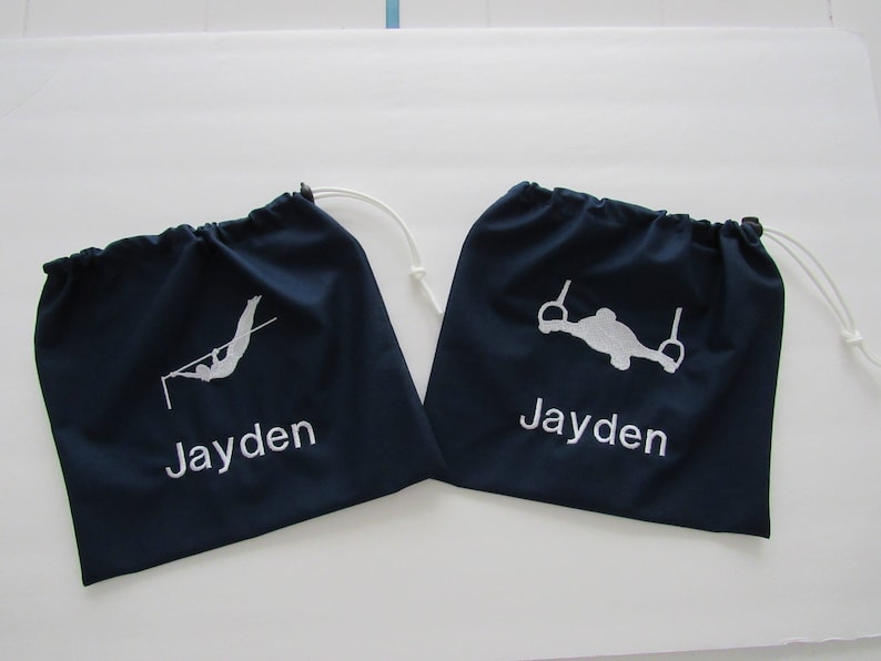May include: Two dark blue drawstring bags with white embroidery. One bag features a silhouette of a person on a high bar and the name "Jayden". The other bag features a silhouette of a person on rings and the name "Jayden".
