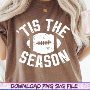 May include: Brown t-shirt with the text "'TIS THE SEASON" in white, featuring a football graphic. The shirt has a vintage, distressed look. The bottom of the image includes the text "DOWNLOAD PNG SVG FILE".