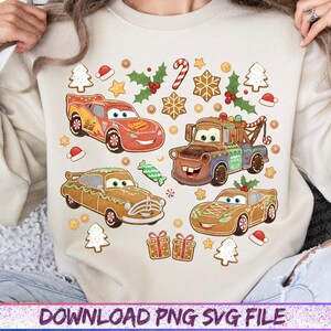 May include: A beige sweatshirt featuring a festive design with cartoon cars decorated as gingerbread and Christmas elements. The design includes red, brown, and green cars, gingerbread cookies, candy canes, and holly.