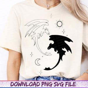 May include: Cream-colored t-shirt featuring a black and white dragon design. One dragon is outlined, the other is solid black. The design includes a sun, moon, and stars. The text "DOWNLOAD PNG SVG FILE" is at the bottom.