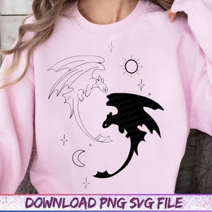 May include: A light pink sweatshirt featuring a black and white dragon design. One dragon is a black silhouette, the other is an outline. The design includes a sun, moon, and stars. The text "DOWNLOAD PNG SVG FILE" is at the bottom.