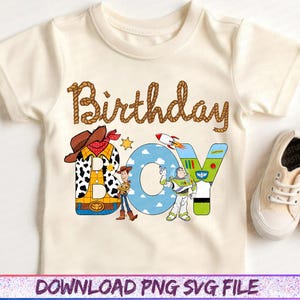May include: Cream-colored short-sleeved t-shirt with the words "Birthday Boy" in brown rope-style lettering. The word "BOY" features cartoon characters and a rocket ship. A pair of beige sneakers are on the right.