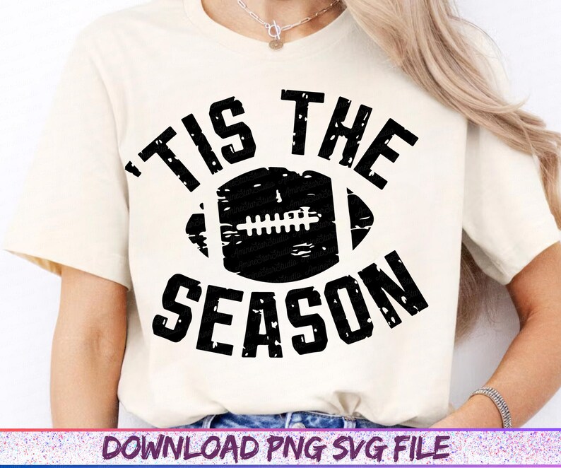 May include: Cream-colored t-shirt with a distressed black football graphic and the words "TIS THE SEASON". The design is centered on the shirt, perfect for football fans.