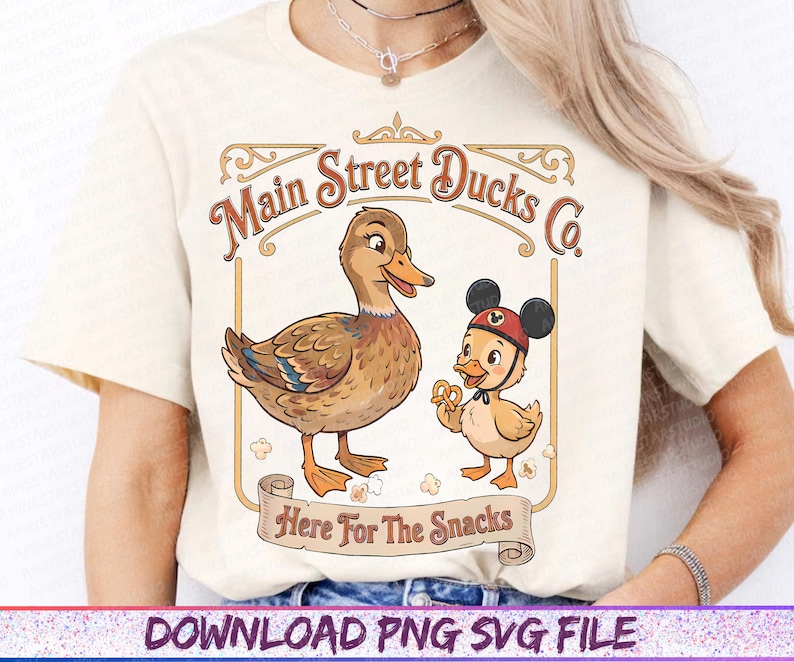 May include: Cream-colored t-shirt featuring a vintage-style graphic. The design includes two cartoon ducks, one wearing a Mickey Mouse hat, and the text "Main Street Ducks Co." and "Here For The Snacks" in a decorative frame.