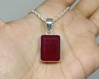 May include: A rectangular, deep red gemstone pendant set in a silver-toned metal frame, suspended from a silver-toned rope chain. The pendant features a faceted surface and is attached to the chain by a simple, polished silver-toned metal bail.