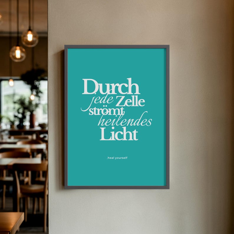 May include: A framed teal print with white text that reads "Durch jede Zelle str&ouml;mt heilendes Licht" and "heal yourself". The frame is dark grey. The print is hanging on a neutral-coloured wall.
