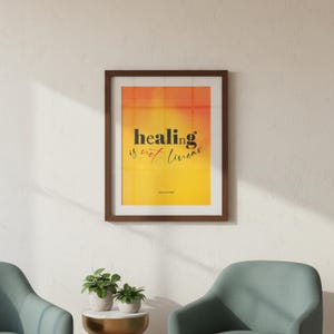 May include: A framed print with the words "healing is not linear" in black text against a yellow and orange gradient background. The print is in a brown wooden frame and is hanging on a white wall.