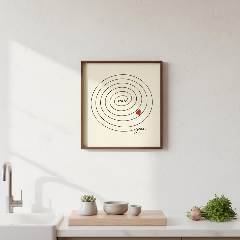 Op de afbeelding: Ingelijste print met een cr&egrave;mekleurige achtergrond. Het kunstwerk heeft een zwart spiraalontwerp met de woorden "me" en "you" en een klein rood hart. De lijst is donkerbruin.