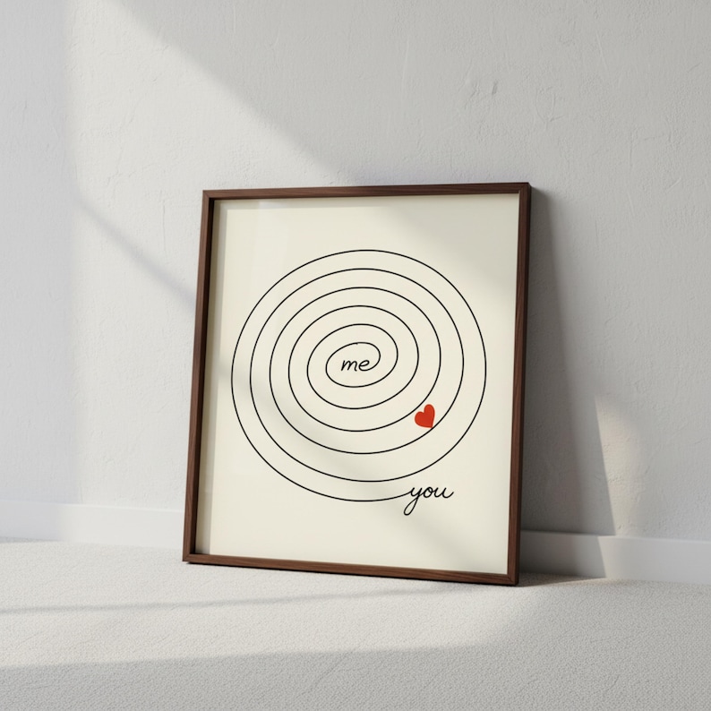 Op de afbeelding: Ingelijste kunstdruk met een minimalistisch ontwerp. Een zwarte spiraal omcirkelt het woord "me" en een rood hart, met het woord "you" onderaan. De lijst is bruin en de achtergrond is gebroken wit.