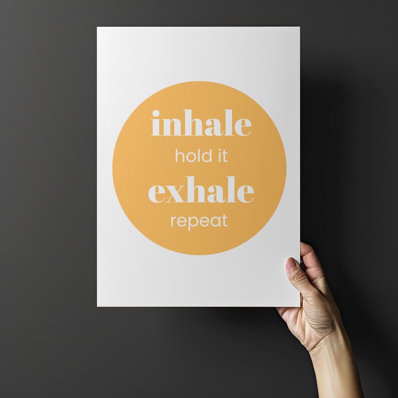 Peut inclure: Une affiche blanche avec un grand cercle orange au centre. Les mots "inhale, hold it, exhale, repeat" sont imprim&eacute;s en blanc, centr&eacute;s dans le cercle. L'affiche est tenue par une main sur un fond gris fonc&eacute;.
