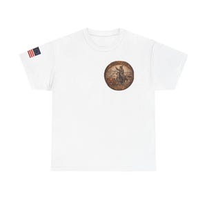 May include: White t-shirt featuring a circular graphic with a historical scene and the text "Rendezvous". An American flag patch is on the left sleeve. The shirt is made of a soft, comfortable material.