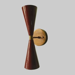 May include: A retro-style wall sconce with a double-cone design. The sconce has burgundy shades and a brass-coloured mounting plate and band. The light fixture is designed for wall mounting, and is a stylish addition to any room.