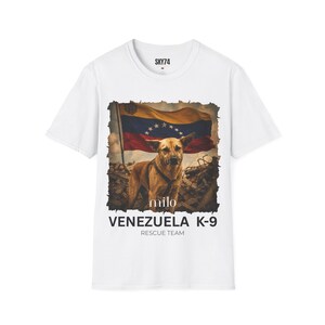 May include: A white short-sleeve t-shirt featuring a graphic print of a brown dog wearing a harness in front of a Venezuelan flag and rubble. The text reads SKY74 at the collar, milo below the dog, and VENEZUELA K-9 RESCUE TEAM at the bottom.
