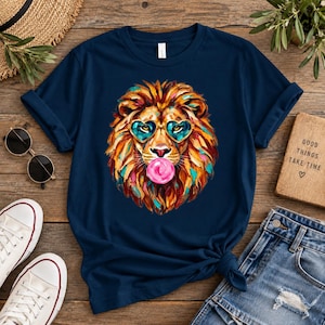 Könnte beinhalten: Ein marineblaues T-Shirt mit einer farbenfrohen Grafik eines Löwen, der herzförmige Sonnenbrillen trägt und eine rosa Kaugummiblase bläst. Die Mähne des Löwen ist in lebhaften Orange-, Gelb- und Türkistönen mit sichtbaren Pinselstrichstrukturen gehalten.
