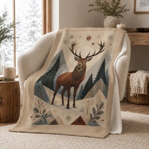 Può includere: Una coperta beige con un'illustrazione centrale di un cervo marrone con grandi corna, in piedi in un paesaggio innevato con pini verde scuro, forme geometriche di montagne e piccoli fiocchi di neve nei toni del rosso e del blu.