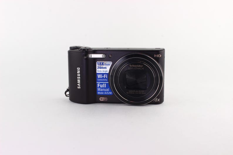 Puede incluir: C&aacute;mara digital Samsung negra con zoom 18x y conectividad Wi-Fi. La c&aacute;mara cuenta con una lente Schneider y un modo manual completo. La c&aacute;mara tiene una lente gran angular de 24 mm.