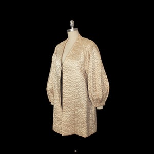 May include: A long, cream-colored quilted jacket with a V-neck and long sleeves. The jacket has a textured, wavy pattern.