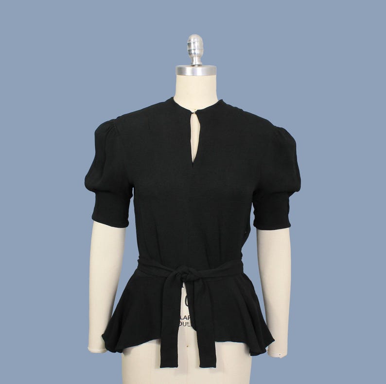 May include: A black, short-sleeved blouse with a fitted bodice and a gathered, flowing skirt. The blouse has a keyhole neckline and a self-tie belt.