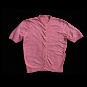 May include: A pink short-sleeved cardigan with a button-up front.